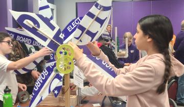 Young student is adjusting wind turbine blades with other students working on other turbines in background