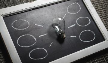 Lightbulb laying on center of chalkboard with six lines leading to six circles drawn on it.