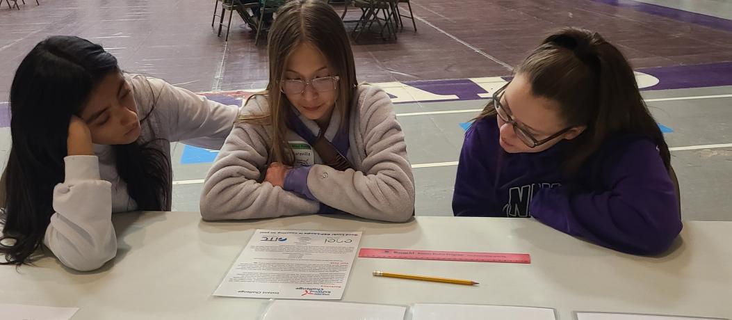 Three students sitting at table looking at documents.